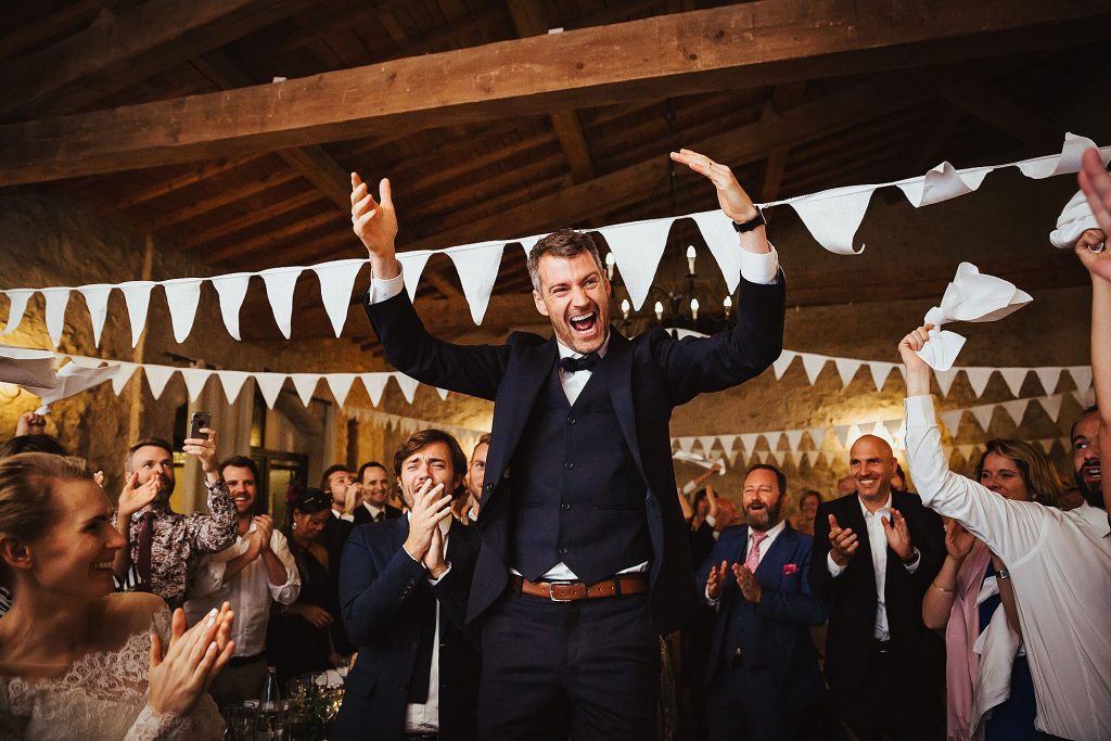 groom cheers as he stands on a chair at Domaine Fon de Rey Wedding